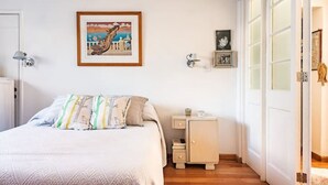 A bedroom with a bed, a nightstand, a framed picture on the wall, and a door with frosted glass panels.