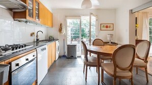 A modern kitchen with a gas stove, oven, and dishwasher. There is a dining table with chairs and a window providing natural light.