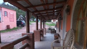 A covered outdoor area with brick pillars, a wooden bench, and a rustic chair. - Posada Margarito (Urique)