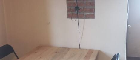 Una habitación con una mesa de madera y dos sillas, un televisor montado en una pared de ladrillo y un suelo de baldosas.