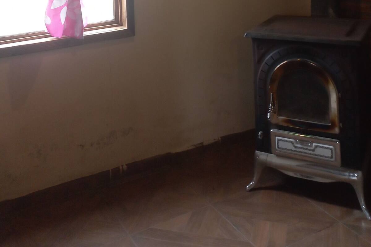 Ein Zimmer mit Fenster, einer grünen Leuchte, einer Backsteinwand und einem Kaminofen.