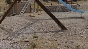A playground with a slide and swings, surrounded by a rocky terrain and trees. - Posada Margarito (Urique)