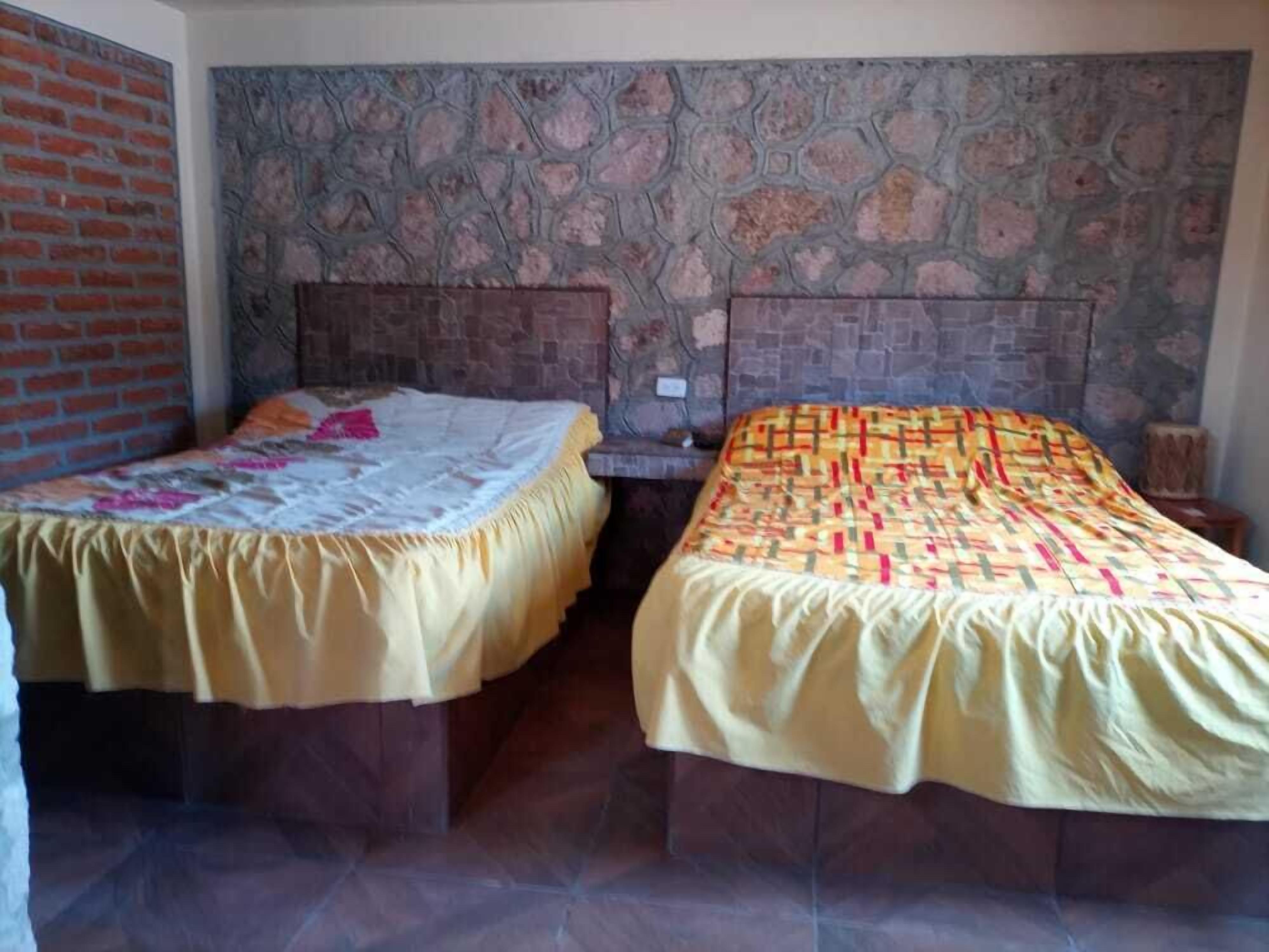 Habitación con dos camas, cada una con una colcha de diseño diferente. Las paredes están decoradas con un papel tapiz de textura que imita a la piedra.
