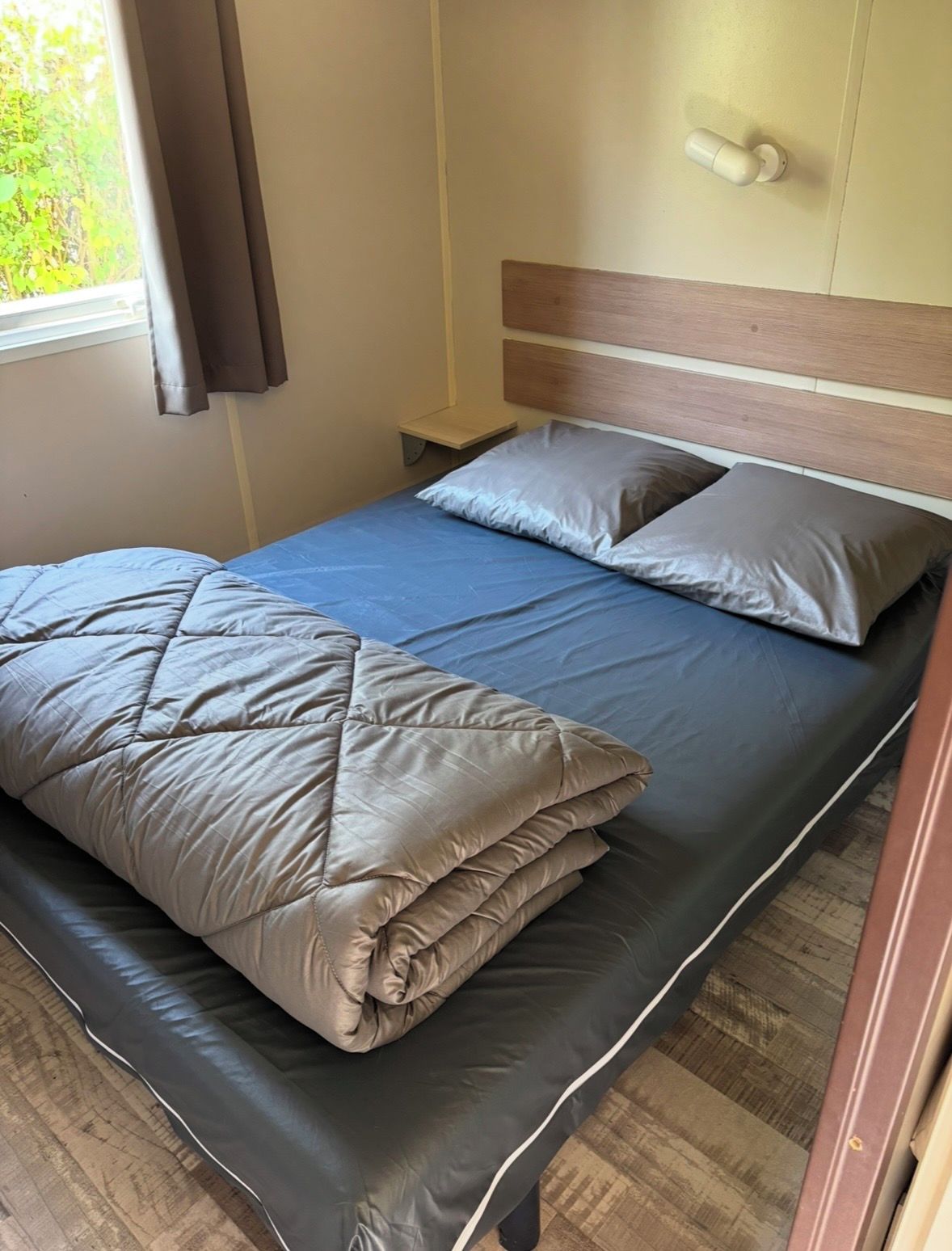 A single bed with a wooden headboard, a bedside table, and a window with curtains.