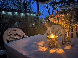 Une table dressée à l’extérieur, avec une bougie, des chaises et un vase de fleurs.
