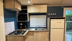 A compact kitchen with a gas stove, microwave, sink, and a refrigerator. - Mobile Home Dans Camping Calme (Biesheim)