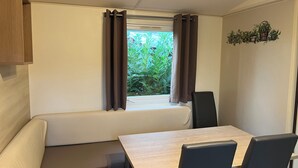 A compact room with a window, a bench, a table, and two chairs. - Mobile Home Dans Camping Calme (Biesheim)