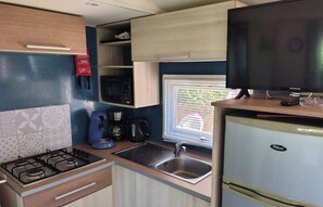 Cocina compacta con estufa a gas, pileta, refrigerador, microondas y televisor.