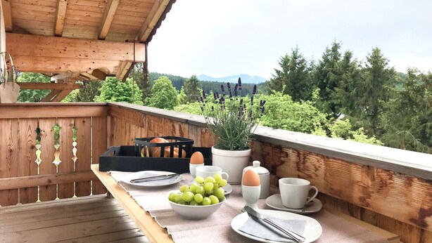 Ein Holzbalkon mit einem Frühstückstisch, gedeckt mit Brot, Trauben, Eiern und Tassen.