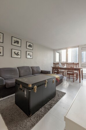 Un salon avec un canapé, une table à manger et des chaises, une malle noire et des tableaux encadrés accrochés au mur.