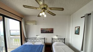 Een kamer met twee bedden, een plafondventilator, een schilderij en een raam.