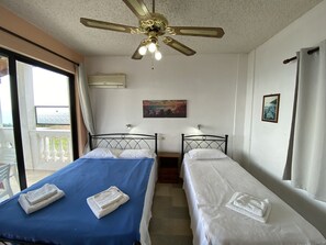 A room with two beds, a ceiling fan, a painting, and a window.