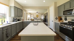 A spacious kitchen with grey cabinets, a central island, a stove, and a microwave.