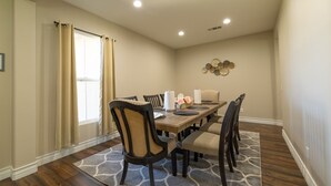 A dining room with a wooden table, beige curtains, and a patterned rug.