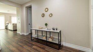 A hallway with a wooden floor, a white door, and a console table with books and decorative items.