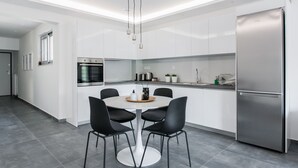 A modern kitchen with white cabinets, a stainless steel refrigerator, and a dining area with a round table and black chairs. - Stellar 3BR Apartment with Balcony (Paleo Faliro)