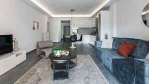A modern living room with a sofa, a coffee table, a TV, and a kitchen in the background. - Stellar 3BR Apartment with Balcony (Paleo Faliro)