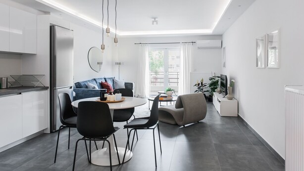 A modern kitchen with white cabinets, a built-in refrigerator, and a dining area with a round table and chairs. - Stellar 3BR Apartment with Balcony (Paleo Faliro)