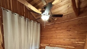 Una habitación acogedora con paredes de madera y un ventilador de techo, que incluye un sofá y una cortina.