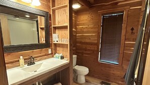 Baño de cabaña de madera con lavamanos, espejo, inodoro y ventana.