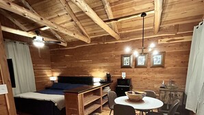 Interior de una cabaña de madera con cama, una mesa de comedor con sillas, un microondas y una pequeña cocina.