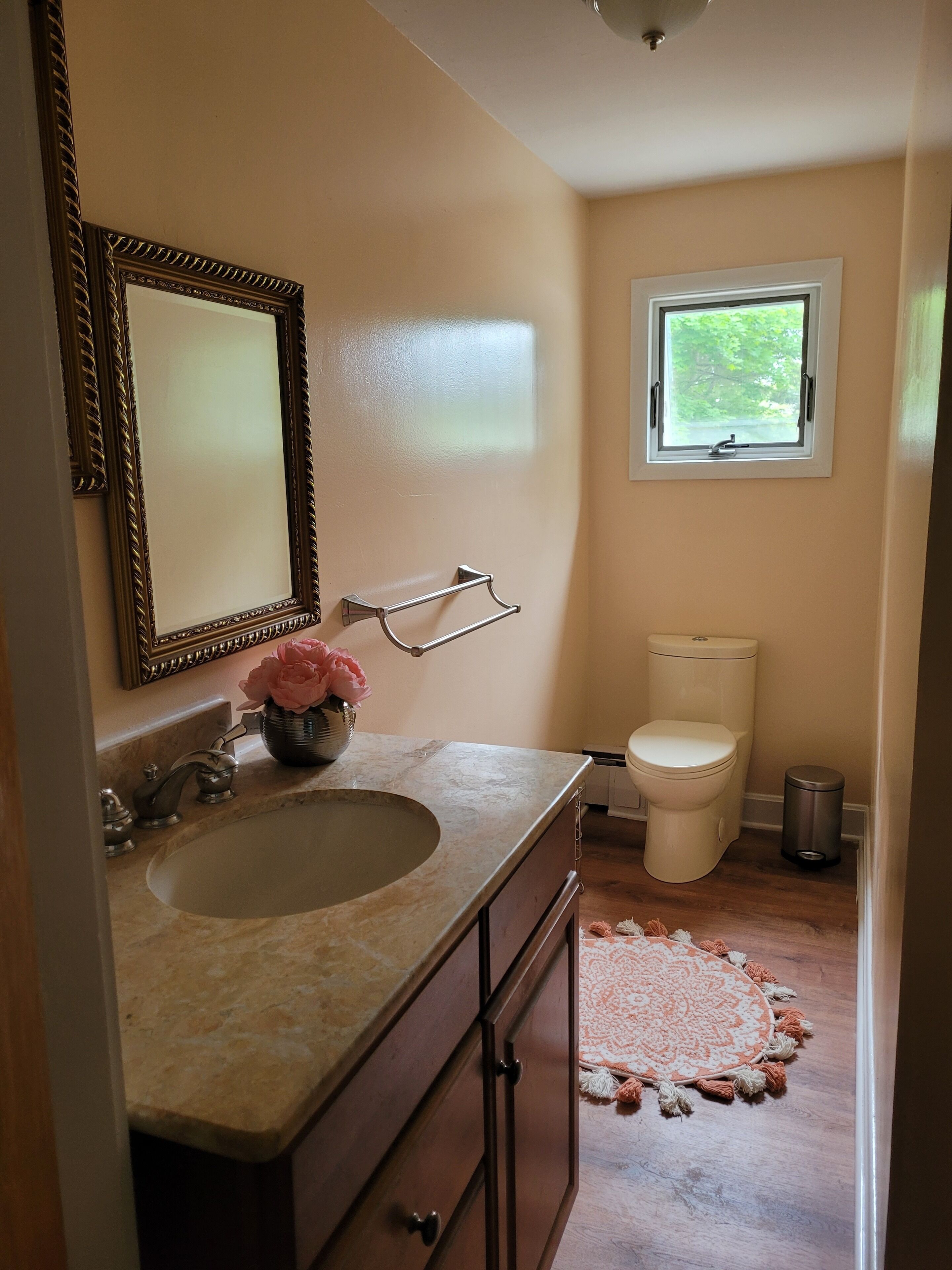 A bathroom with a sink, mirror, toilet, and window.