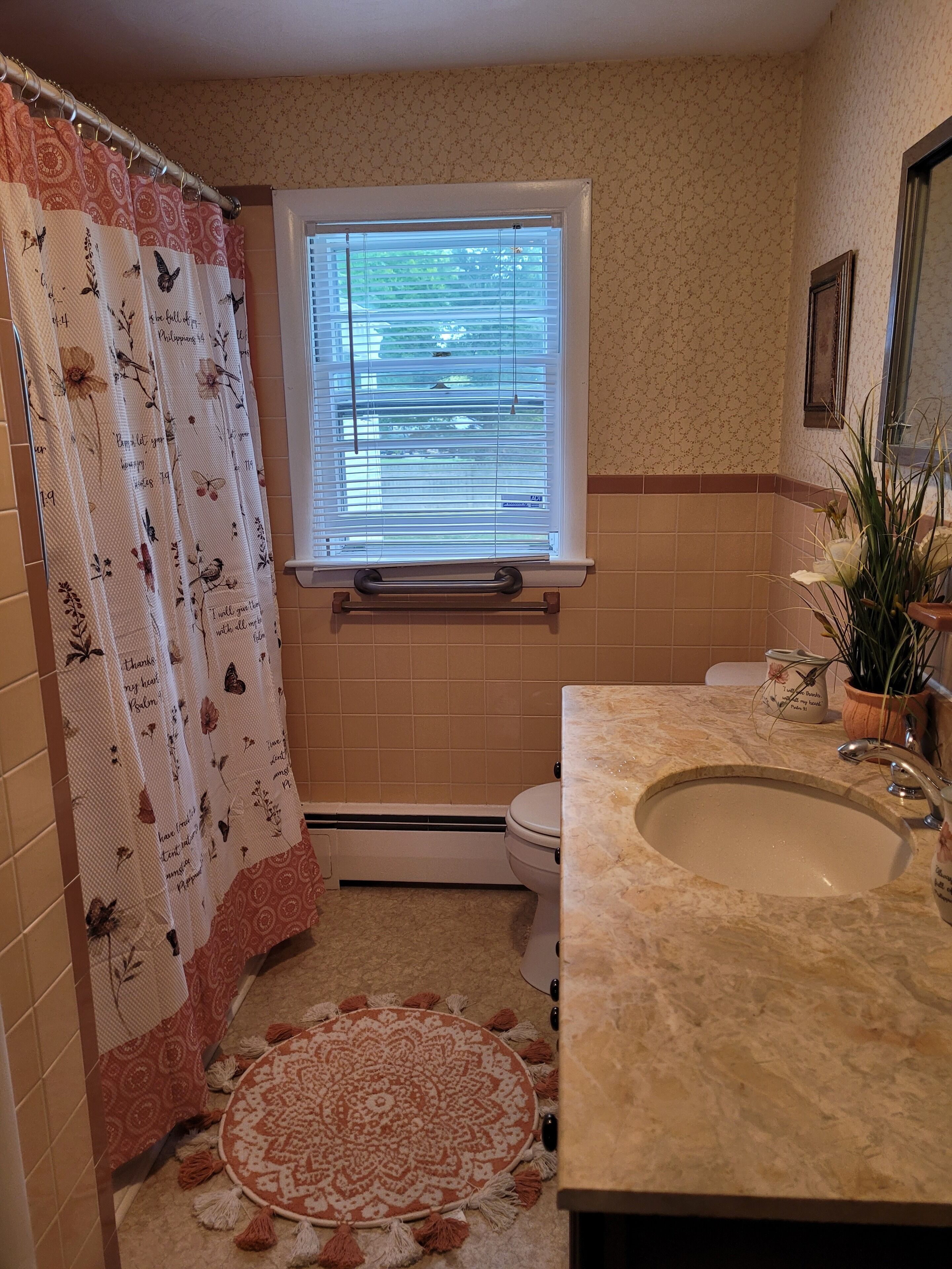 A bathroom with a window, a sink, a toilet, and a shower curtain with floral patterns.