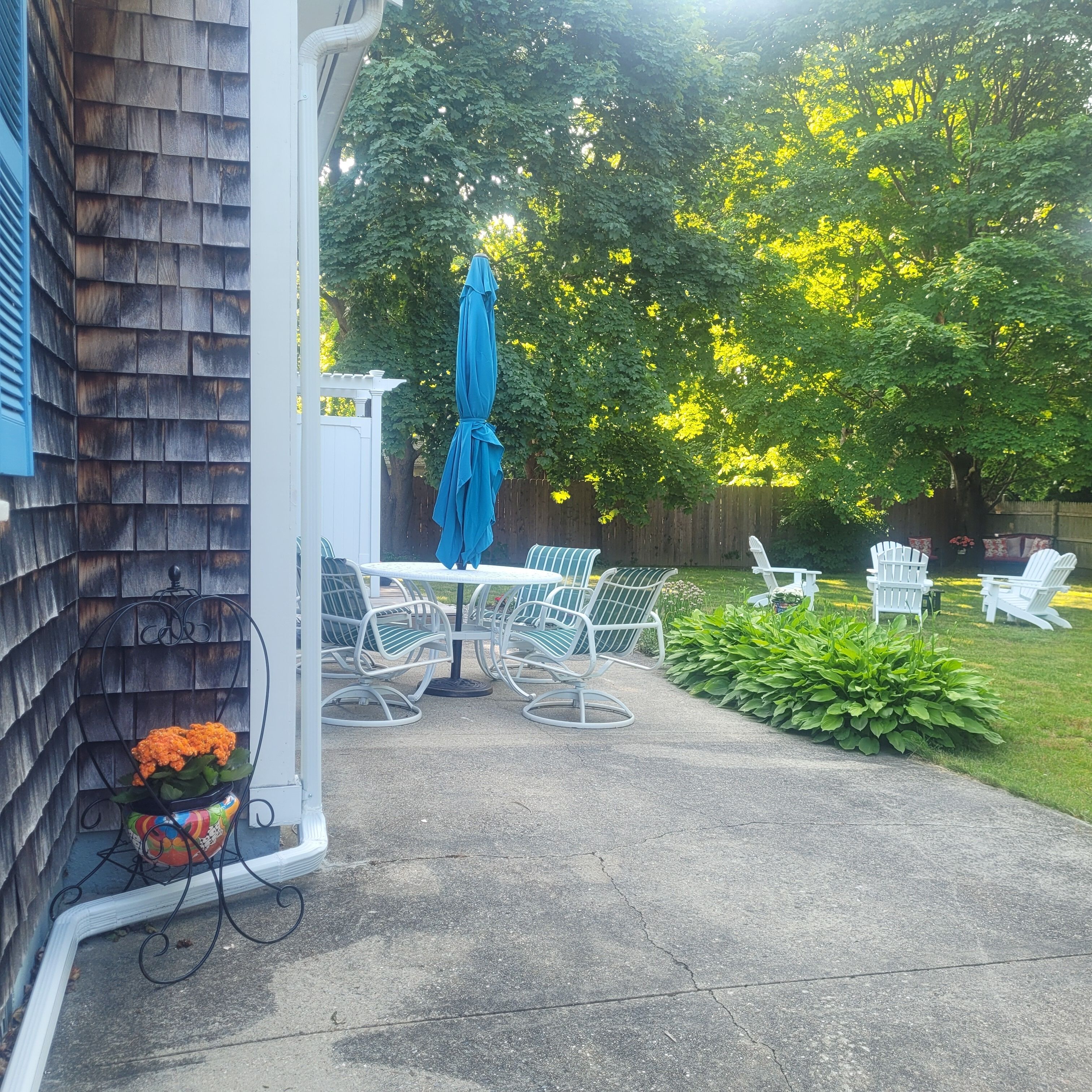 Une terrasse avec une table et des chaises, un parasol bleu et un coin jardin aménagé avec des sièges.