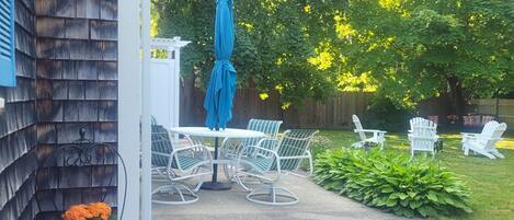 Une terrasse avec une table et des chaises, un parasol bleu et un coin jardin aménagé avec des sièges.