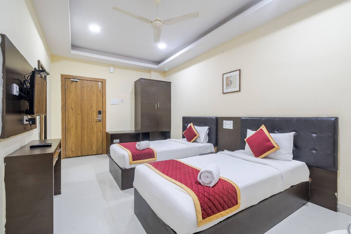 A hotel room with two beds, a wardrobe, a desk, and a ceiling fan.