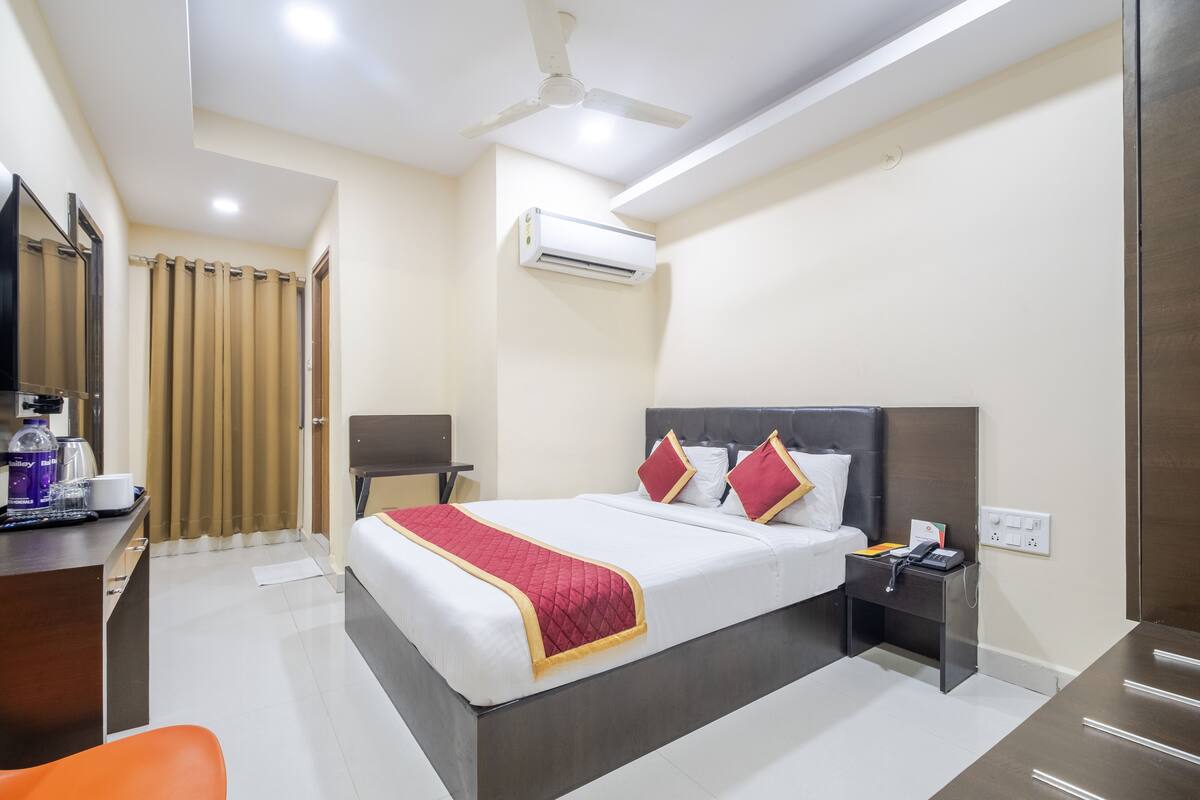 A hotel room with a bed, bedside table, desk, chair, and an air conditioning unit.