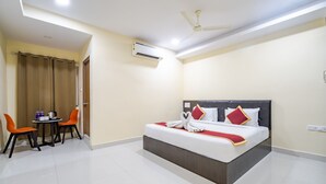 Une chambre d’hôtel équipée d’un lit, d’un bureau avec des chaises, d’un climatiseur et d’un ventilateur de plafond.