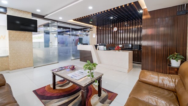 Un hall d’hôtel moderne avec un comptoir d’accueil, des canapés en cuir, une table basse avec un menu, et une grande fenêtre.