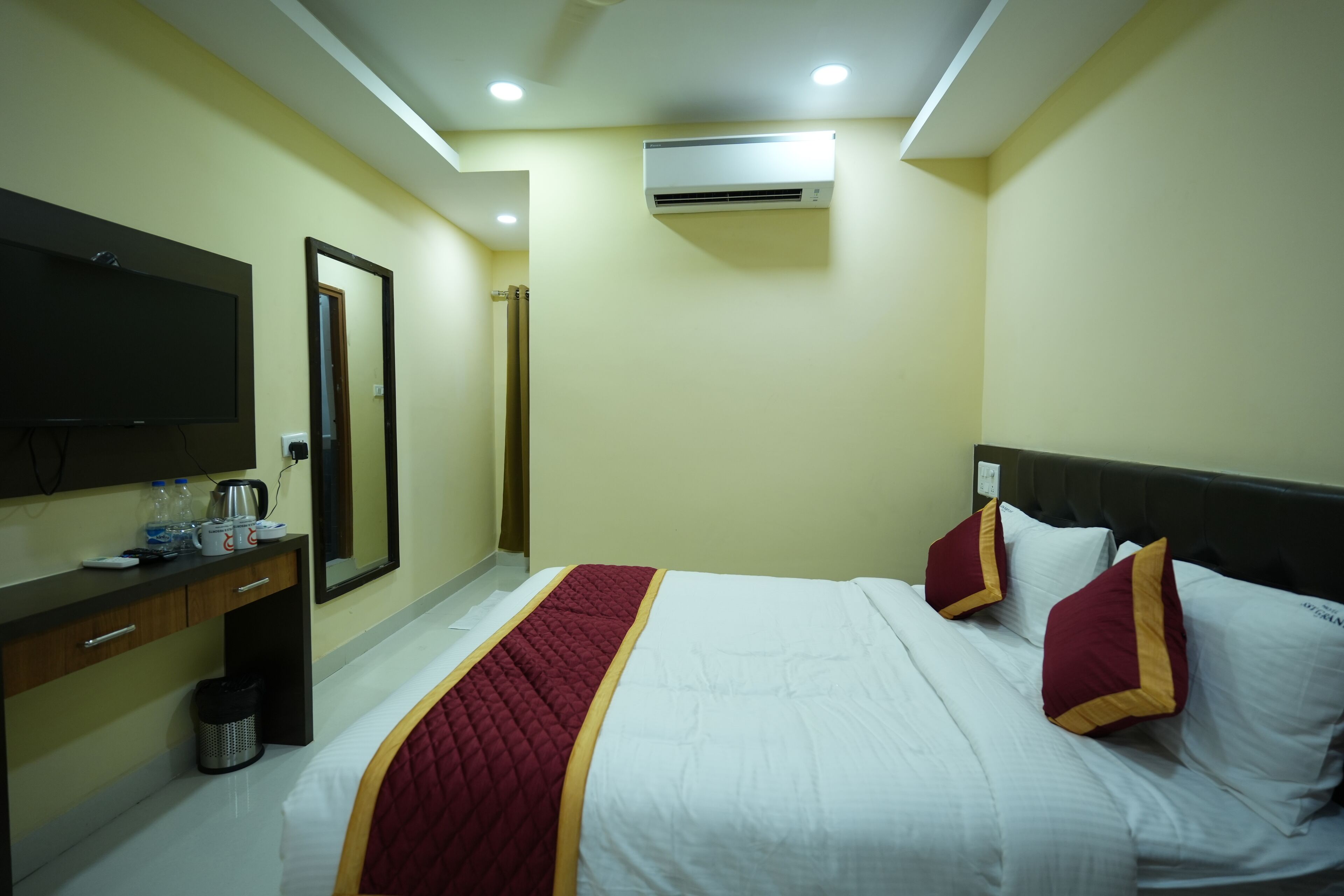 Habitación de hotel con cama, televisión, escritorio con espejo y aire acondicionado.
