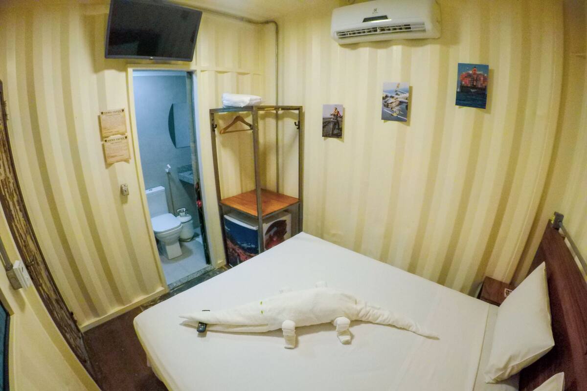 Une chambre d’hôtel équipée d’un lit, d’une petite table, d’un fauteuil suspendu, de toilettes et d’un appareil de climatisation.