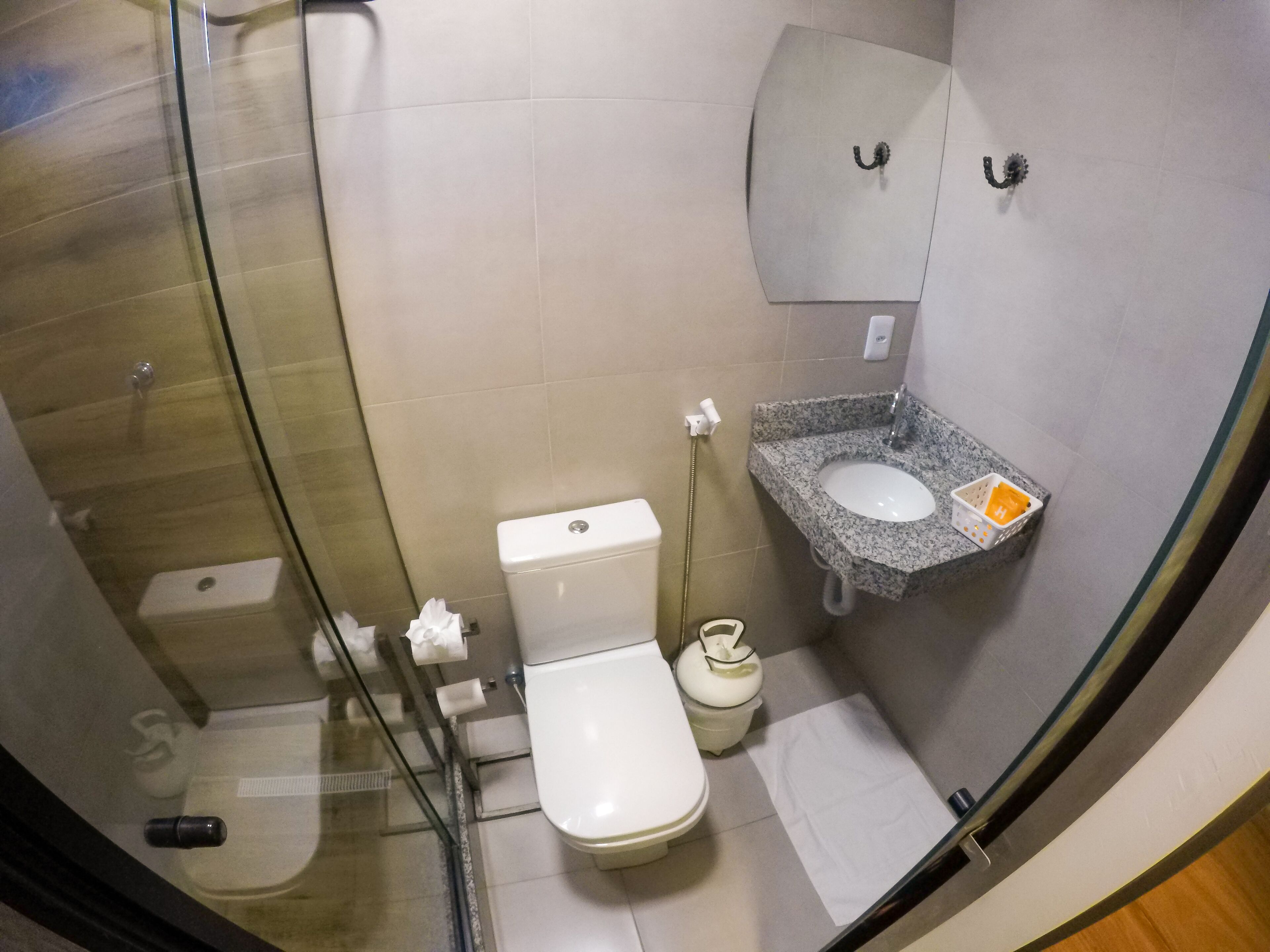 A compact bathroom with a glass-enclosed shower, a white toilet, and a granite sink with a soap dispenser.