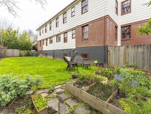 Un jardin arrière d’une maison, avec une pelouse verdoyante, des plates-bandes surélevées et une clôture en bois.