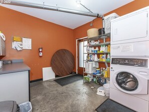 A laundry room with a washing machine, shelves with cleaning supplies, a fire extinguisher, and a bulletin board.