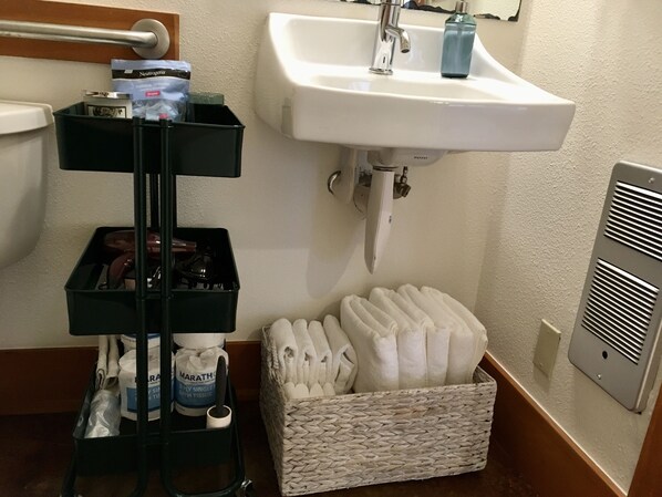 A bathroom with a white sink, a black storage cart with toiletries, and a woven basket with towels.