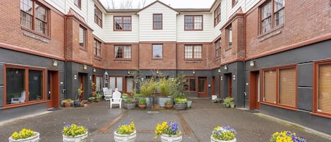 A courtyard with a central seating area, surrounded by brick buildings with large windows and doors.