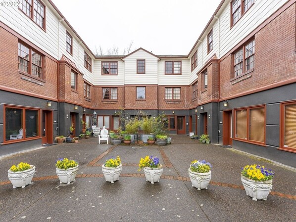 Une cour intérieure dotée d’un espace de repos central, entourée d’immeubles en briques avec de grandes fenêtres et des portes.