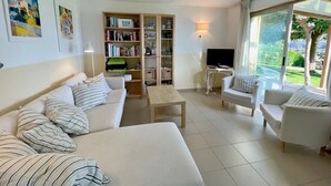 A modern living room with a sofa, armchairs, a coffee table, a bookshelf, and a TV.