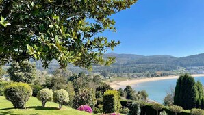 A landscaped garden with manicured hedges and flowering plants, a clear blue sky, and a distant beach view.