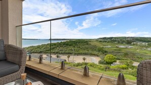 Ein Balkon mit Blick auf einen Strand, Grünflächen und eine entfernte Stadt.