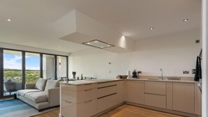 Eine moderne Küche mit einer großen Kochinsel, einem Essbereich mit einer Couch und Blick ins Freie.