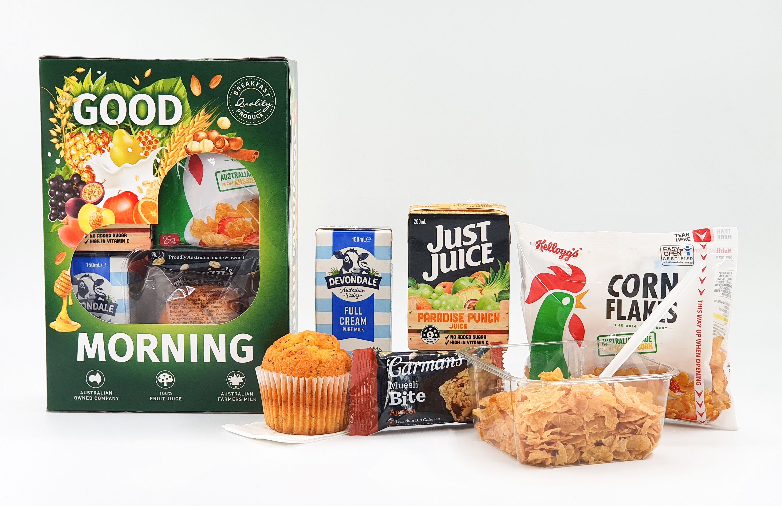 Variedad de productos para el desayuno, incluyendo un cartón de leche Good Morning, leche entera Devondale, Just Juice, Corn Flakes, un muffin y una barra de cereal.