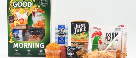 Variedad de productos para el desayuno, incluyendo un cartón de leche Good Morning, leche entera Devondale, Just Juice, Corn Flakes, un muffin y una barra de cereal.