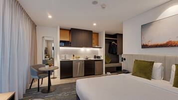 A modern hotel room with a large bed, a small dining area, a built-in closet, and a bathroom.