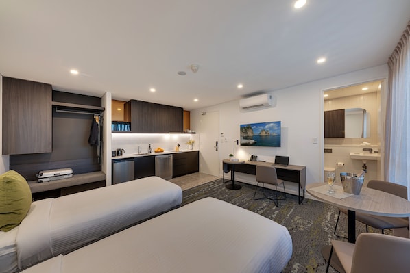 A hotel room with two beds, a kitchenette, a desk, a dining area, and a bathroom. - Littomore Suites Kingswood (Kingswood)