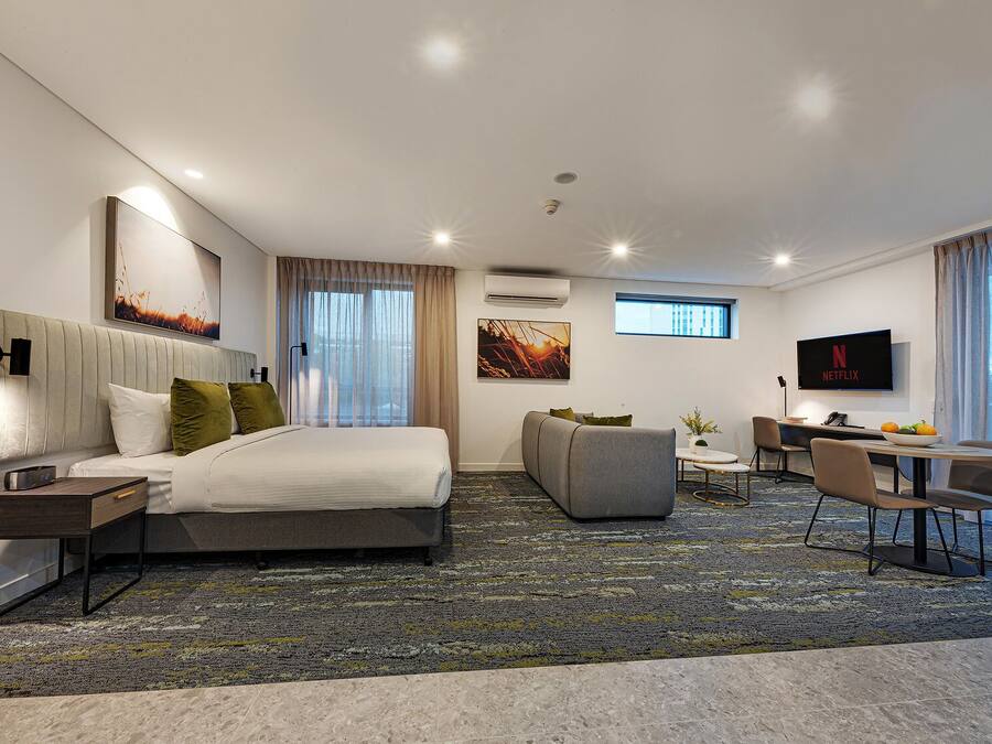 A modern hotel room with a large bed, a sofa, a desk, and a TV.